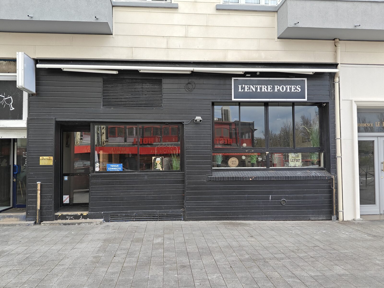 Avant : la façade en bardage noir du bar L'Entre Potes et sa petite enseigne rectangulaire