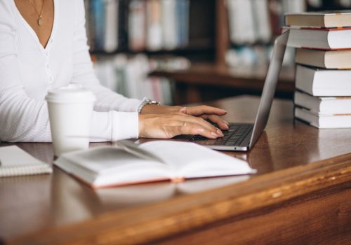 Young woman sitting at the library using books and computer